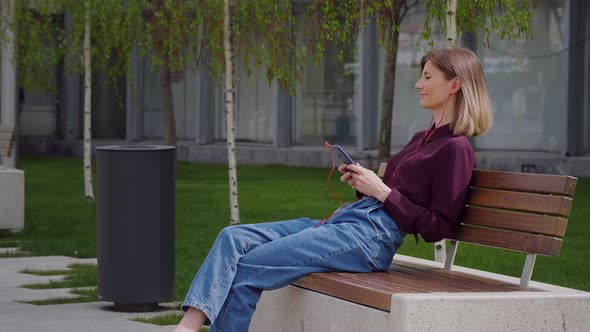 Woman sitting on a bench Using Headphones to listen to Music.