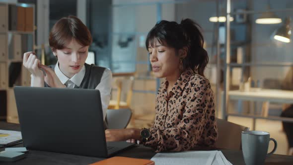 Young Businesswomen Discussing Project on Laptop in Office at Night