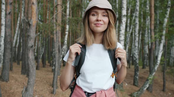 Portrait of Cheerful Female Tourist with Backpack Standing in Wild Woods Smiling