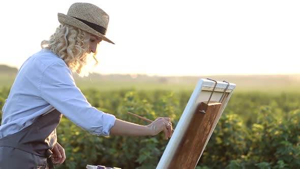 The young artist paints a summer landscape. The girl in the nature of the artist paints