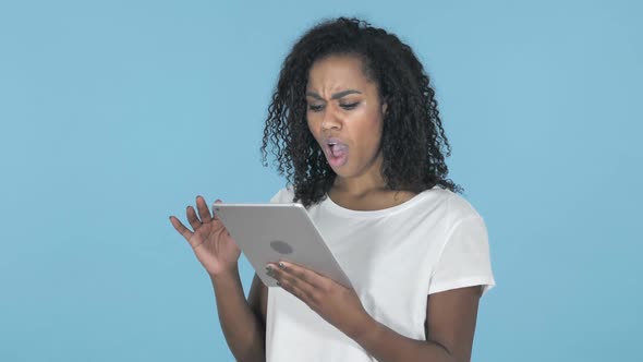 African Girl in Shock While Using Tablet Isolated on Blue Background