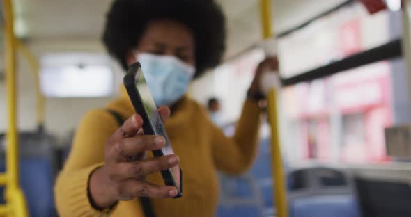 African american businesswoman with face mask using smartphone and standing in bus