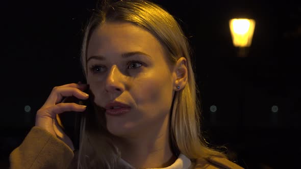 A Young Beautiful Woman Talks on a Smartphone in an Urban Area at Night 