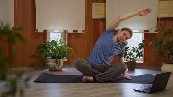 Front View of Young Man Doing Stretching Exercises with Online Yoga Trainer Via Internet