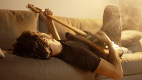Man Playing on Guitar While Lying on Couch in Smoky Room