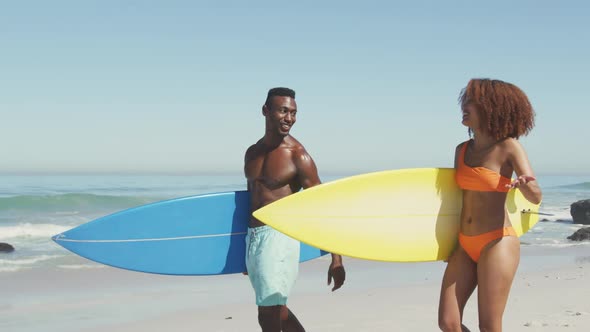 African American couple walking and holding surfboards