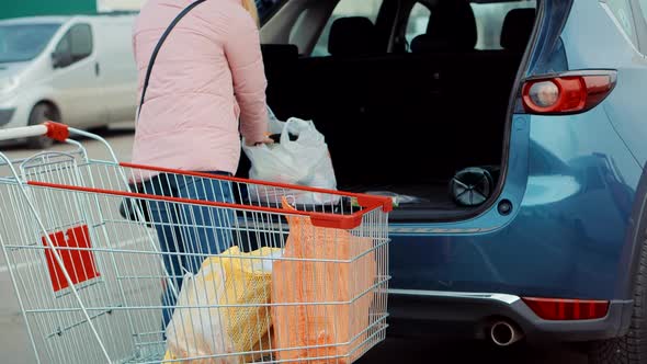 Puts Bags In Trunk Of Car In Mall Parking Lot. Woman Putting Shopping Bags Inside Trunk Supermarket.