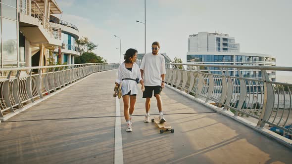 Millennial Couple in Love Enjoying Evening Walk with Skateboards