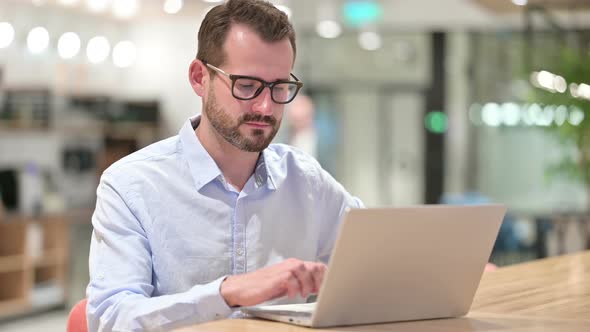 Businessman with Laptop Smiling at Camera in Office 