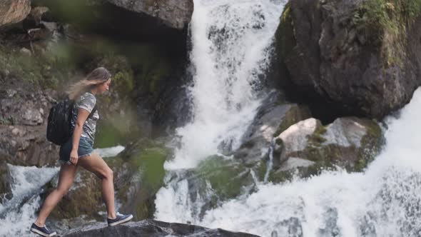 A Female Tourist with a Backpack Climbs Onto the Edge of a Cliff and Raises His Hands Up in Front of