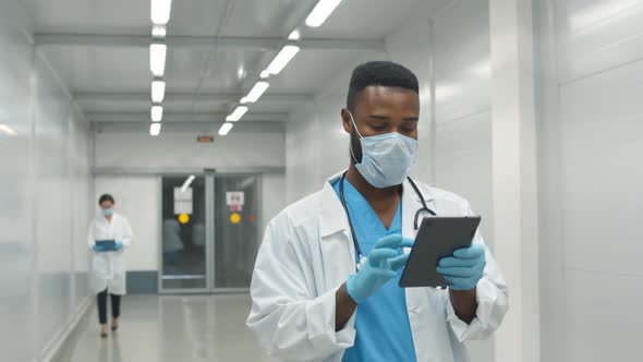 African Doctor Wearing Protective Mask and Gloves Using Tablet Working in Clinic