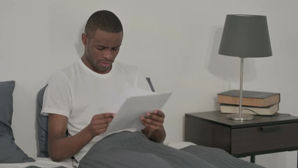 African Man Upset While Reading Documents in Bed