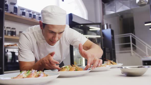 Mixed race male chef wearing chefs whites in a restaurant kitchen, putting food on a plate