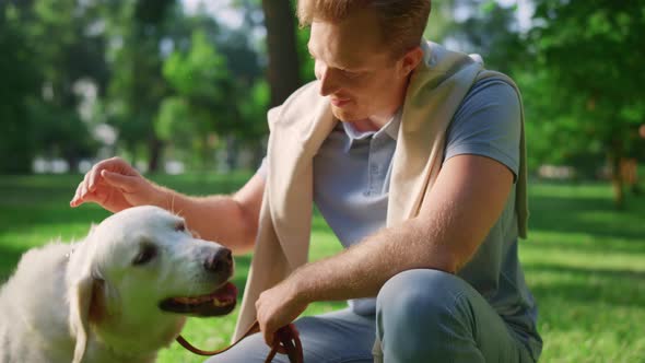 Joyful Smiling Man Petting Golden Retriever in Park