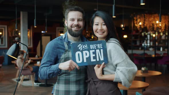 Slow Motion Portrait of Man and Woman Holding Open Sign in Modern Restaurant