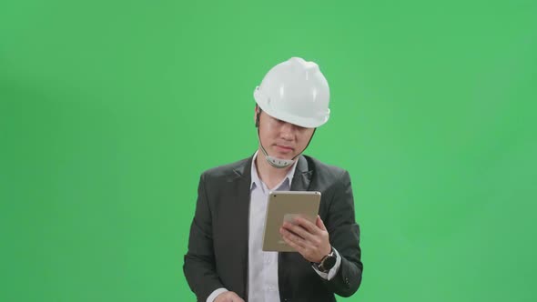 Asian Chief Engineer In The Hard Hat Use Tablet While Walking On Green Screen Chroma Key