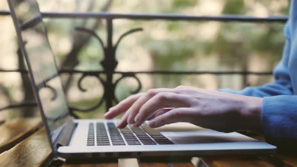 Woman blogger freelancer working on laptop outdoor at street cafe. Close up of hands using keyboard