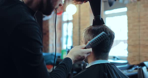 Male Stylist Dries the Hair to a Client Holds a Comb and a Hairdryer