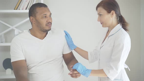 Caucasian Doctor Holding Hand of African American Patient and Talking. Portrait of Professional