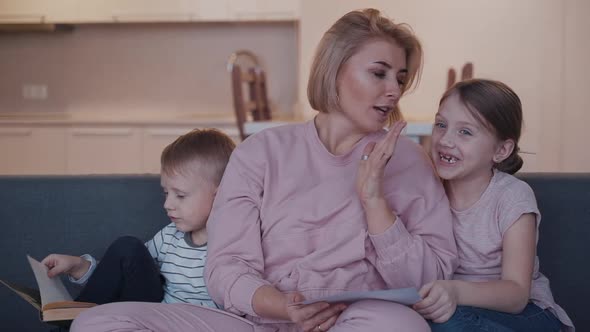 Young Mother Is Talking with Daughter About Her Creative Drawing While Little Brother Is Reading