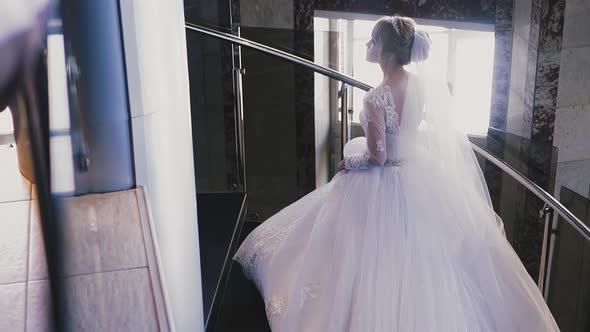 Elegant Bride with Fop and Gorgeous Dress Goes Up Stairs