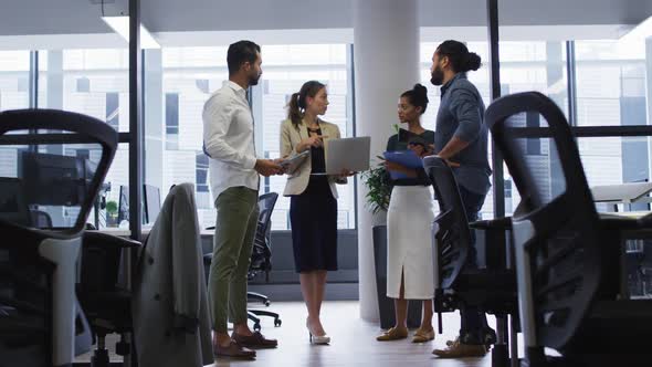 Caucasian businesswoman holding laptop talking to diverse colleagues standing at office meeting