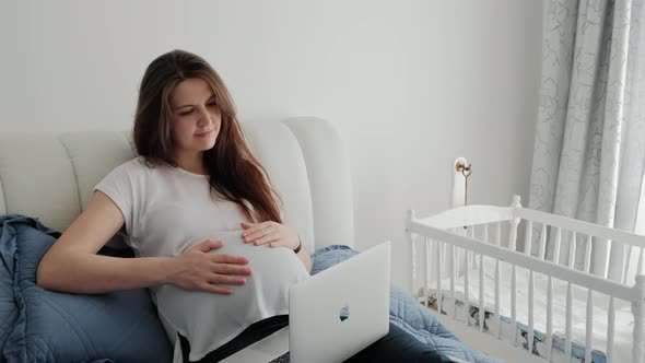 Pregnant Woman Resting on a Sofa at Home and Working with Laptop Computer Using Online Technology