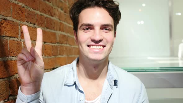 Victory Sign by Handsome Young Man Sitting at Loft Hoe