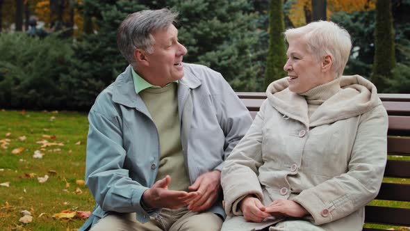 Smiling Elderly Couple Communicate Sit on Bench Man Congratulate Hugging Wife Happy Grandparents