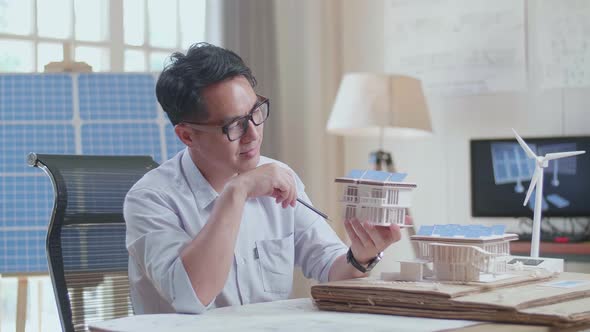 Man Positively Shaking His Head While Holding And Looking At Model Of Small House With Solar Panel