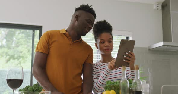 Video of happy african american couple cooking together in kitchen, using tablet