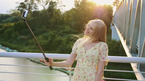 Woman Taking Selfie on Bridge. Cheerful Pretty Blonde Young Lady Standing on Pedestrian Bridge and