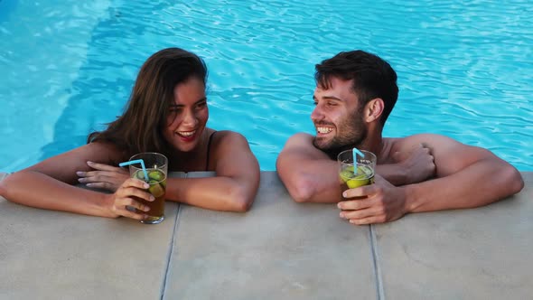 Couple having iced tea while interacting at poolside