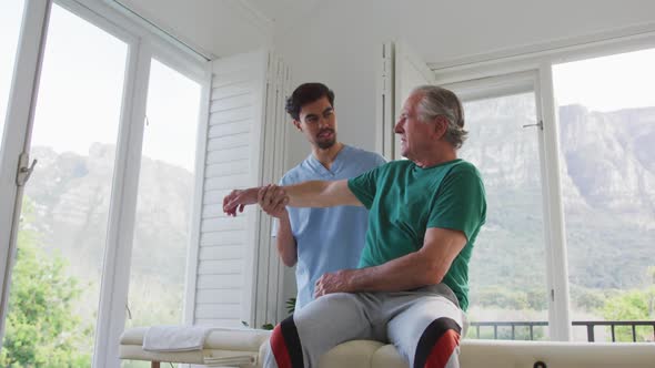 Slow motion shot of male physiotherapist helping senior patient exercising at retirement home