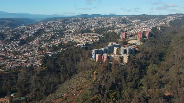 Aerial orbit of colorful buildings in hillside Quinta Vergara Park covered in forest, Viña del Mar c