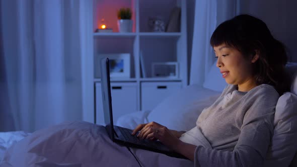 Woman with Laptop in Bed at Home at Night