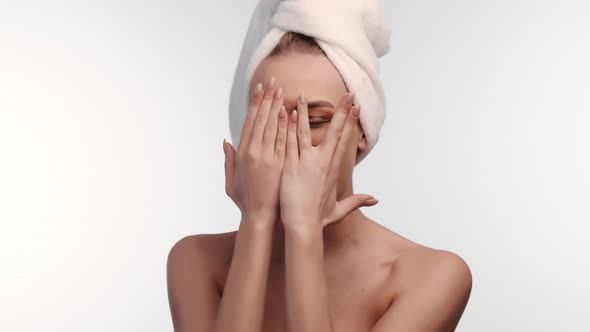 Woman with towel on head hides face behind palms and then removes hands showing clean, beautiful
