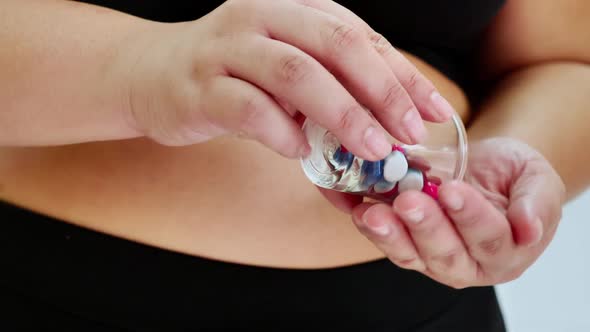 Overweight woman holding diet pills and looking her belly fat into the mirror