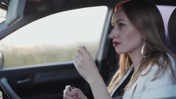 Beautiful Woman Looking in Rear View Mirror and Applying Mascara in Car