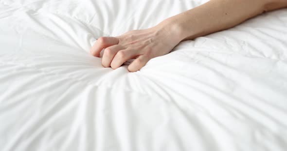 Woman Hand Tightly Squeezes Sheet on Bed