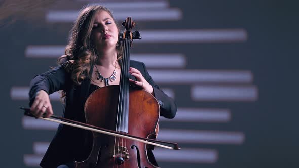 Young Beautiful Woman Playing on Cello in the Spotlight. Grey Background