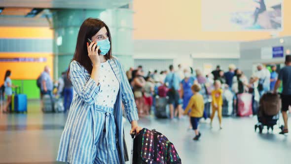 Woman in Mask, Talking on Mobile, Against Background of Air Passengers Crowd, at Airport. Waiting 