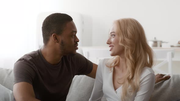 Loving Diverse Couple Talking Sitting On Sofa At Home