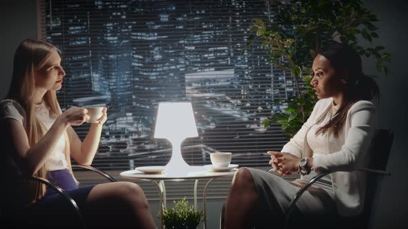 Middle Close Up of Mixed Race Business Women Discussing Something at the Table with a Cup of Drink