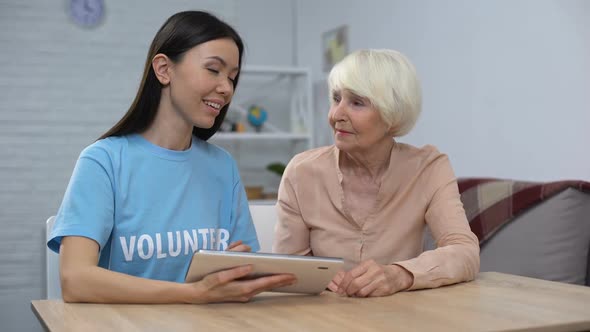 Female Volunteer Showing Elderly Pensioner to Use Tablet App Smiling Camera