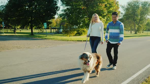 Asian Male and Caucasian Woman Walking in Park with Her Dog