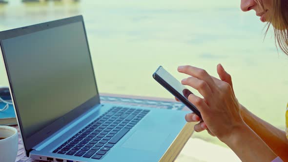 Side View Woman in Hat at Beach with Laptop Using Smartphone Online Chatting Browsing on Internet