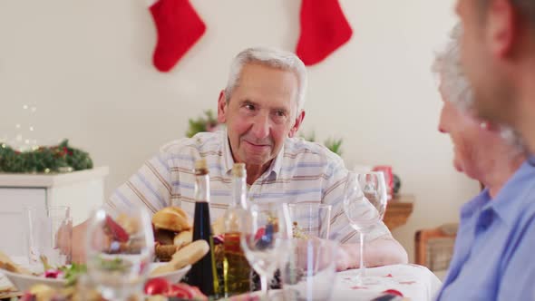 Caucasian senior man talking while sitting on dining table enjoying lunch together during christmas