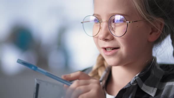 Female Elementary School Student Wearing Glasses Takes Online Lessons with Teacher Via Video Link on