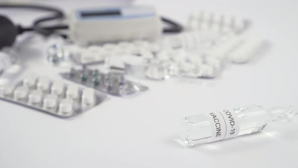 Glass ampoule with medicine rolls on a white table with medical equipment and pills